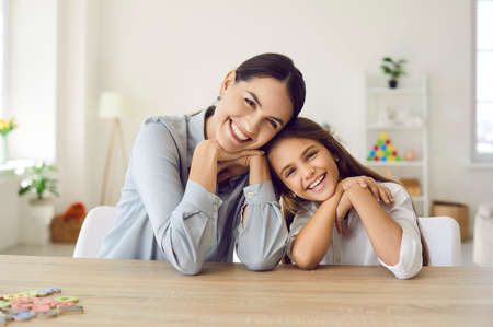 Happy teacher and student girl sitting at working desk in classroom. Cheerful young mother and child...