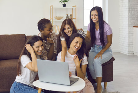 Happy best friends using modern laptop computer together. Cheerful positive young multiethnic women...