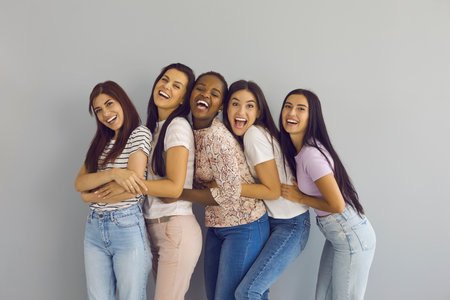 Portrait of smiling young multiethnic diverse girlfriends on gray wall background laugh joke...