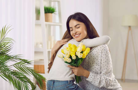 Happy young Caucasian mom hug thank loving small daughter for flowers for mothers day. Caring little...