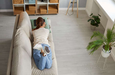 Woman lying on sofa with digital tablet enjoys leisure, watching programs or chatting online. High...