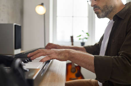Close up of hands of professional male musician playing on synthesizer in music studio. Talented and inspired man plays synthesizer keyboard and concentrates on music. Concept of creating music.の写真素材