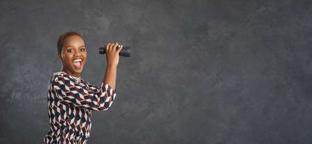Wow, thats cool. Copy space banner background with studio portrait of happy smiling black woman holding binoculars, waiting and looking forward to big sale, bargain, special offer, clearance, blowoutの写真素材