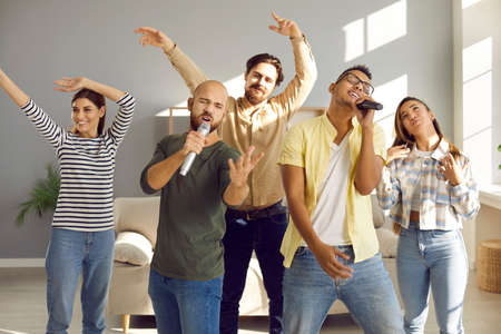 Overjoyed diverse friends have fun on weekend enjoy karaoke together. Smiling multiracial young people relax on leisure day off sing with microphones at home. Hobby and entertainment concept.の写真素材