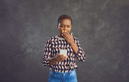 Portrait of an anxious frightened young African American woman looking at the phone in her hands....