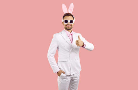 Handsome man with bunny ears wishing you Happy Easter. Happy attractive young guy in white stylish...