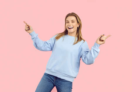 Cheerful teenage girl laughing, having fun and dancing, isolated on pastel pink background. Smiling girl in casual light blue hoodie and jeans celebrating her success. Banner. Copy space.の写真素材