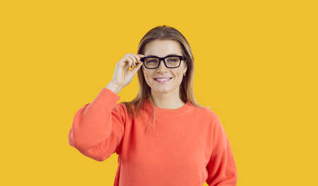 Portrait of young woman with beautiful smile wearing glasses isolated on yellow background....