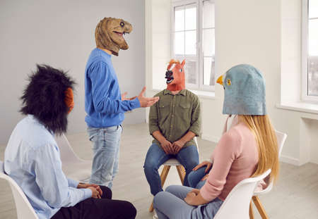 People wearing funny masks having a conversation during a group therapy session. Different male and...