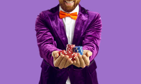 Close up of poker chips in hands of joyful excited man isolated on purple background. Cropped image...