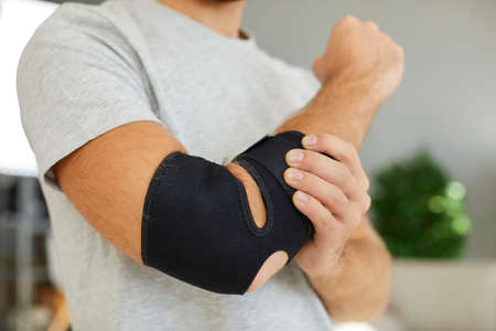 Hand injury. Close up of black elastic supportive medical bandage on elbow of man who is recovering from injury. Man is forced to wear bandage on his arm after broken bone or after sports injury.の写真素材