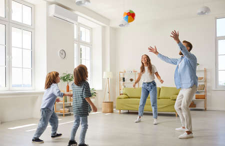 Smiling young Caucasian family with small children relax playing with ball in living room. Happy parents mom and dad have fun relax involved in game activity with kids at home. Active weekend.の写真素材