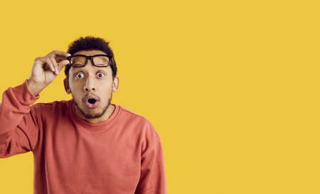 Portrait of funny surprised young man looking at you with shocked expression on yellow background....