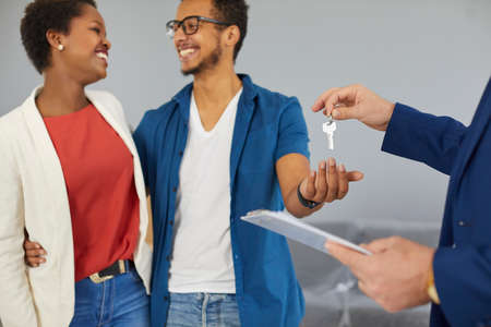 Real estate agent give keys to new home to happy ethnic family buyers. Realtor or broker congratulate multiracial couple clients with house purchase. Property ownership. Rental and realty concept.の写真素材