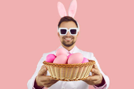 Close up of wicker bowl with painted easter eggs in hands of happy man on pink background. Man with...