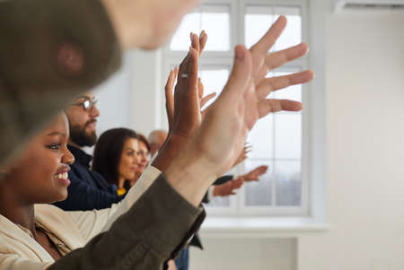 Happy mixed race male and female audience sitting in row and raising hands up. Multiethnic men and women willing to ask questions at interesting seminar session, public presentation or masterclassの写真素材