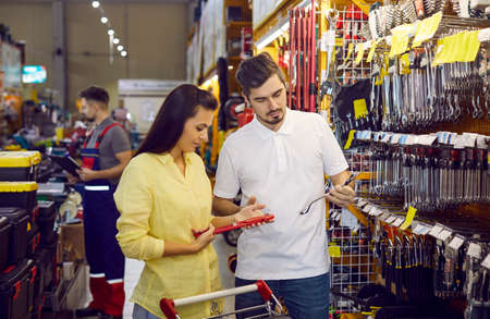 Customers shopping at a DIY store. Young married couple shopping for tools at a modern hardware store. Husband and wife together buying stuff for renovating the house and doing different home repairsの写真素材