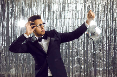 Young black male magician hold discoball isolated on glitter disco background. Amazed African American man entertainer with shiny ball in nightclub have fun. Entertainment concept.の写真素材
