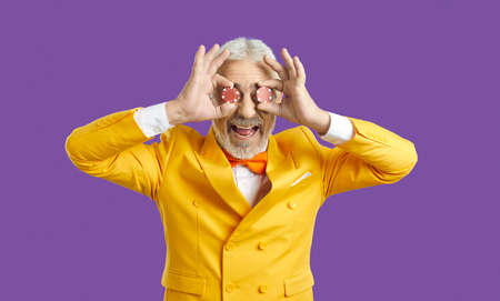 Studio shot of happy funny goofy bearded adult man in funky yellow suit standing isolated on purple...