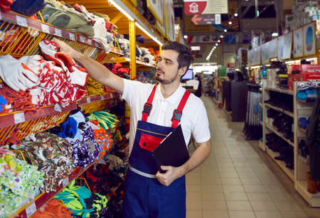 Salesman in uniform work in building hypermarket check products on shelves. Male consultant or assistant work restock goods in household or construction store. Shop assistance and consult.の写真素材