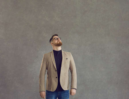 Serious smart caucasian business man looking up studio shot over grey background. Thoughtful office worker, male entrepreneur standing with pensive expression. Planning and contemplationの写真素材