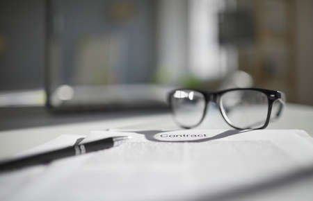 Contract or agreement with pen and eyeglasses on office table. Close up shot. Concept of concluding. Focus on contract paper, blurred background. Business workplace, lawyers workplaceの写真素材