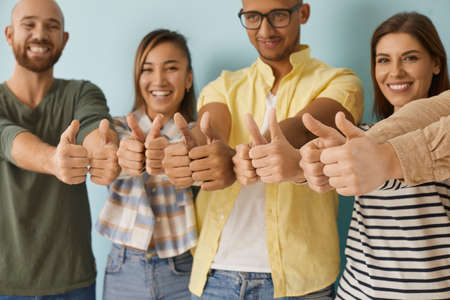 Diverse group of happy cheerful young people showing like gestures all together. Joyful optimistic multiethnic multicultural men and women giving thumbs up and smiling. Close up of human handsの写真素材
