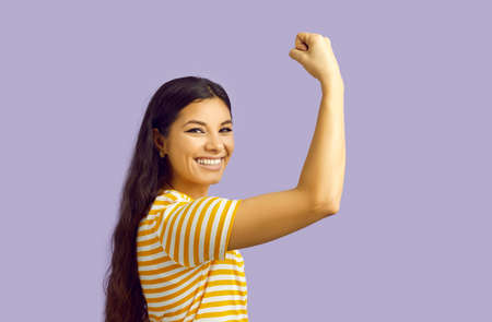 Smiling strong ethnic woman isolated on purple studio background show muscles and power. Happy powerful girl demonstrate strength and leadership. Women can do it.の写真素材