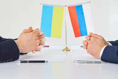 Negotiations between representatives of Ukraine and Russia on resolving military conflict. Close up of male hands on table on background of state flags. Concept of cooperation or opposite conflict.の写真素材