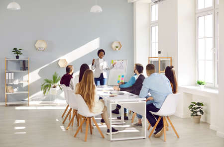 Smiling confident black businesswoman present project on whiteboard for team colleagues. Happy...