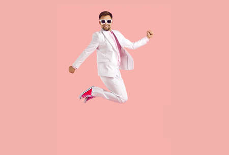 Cheerful funny young man in white suit jumps high isolated on pastel pink background. Stylish cool...