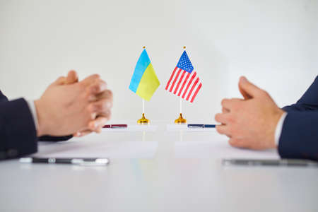 Negotiations between representatives of States. Negotiations on future strategy and relations between Ukraine and United States. Focus on flags of states standing on table near mens hands. Close up.の写真素材