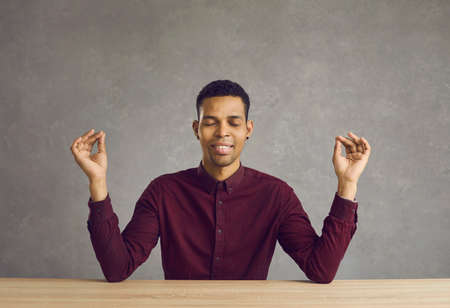 Happy calm young latin man meditating with eyes closed smiling sitting at desk. Business pause, take...