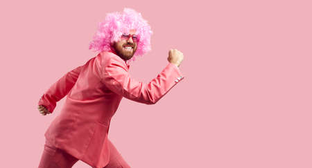 Happy goofy clown having fun in the studio. Funny handsome young man wearing pink wig, trendy suit...