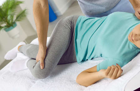 Physical rehabilitation. Male chiropractor or physiotherapist performing adjustment on back of young woman. Cropped image of doctor kneading female patient lying on couch of rehabilitation clinic.の写真素材
