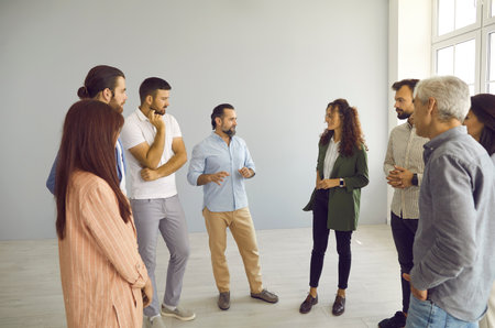 Group of people standing in modern office and talking. Business trainer meeting with team of men and women, having interesting discussion, providing expert guidance and helping find better solutionの写真素材