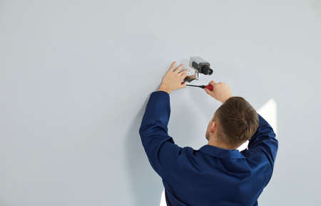 Service for installing cctv cameras. Professional male technician mounts video surveillance camera on wall of house or office. Rear view worker with screwdriver installs security camera. Copy space.の写真素材