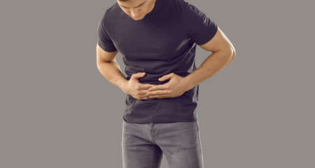 Unhealthy man isolated on grey studio background struggle from stomachache. Pain in belly or stomach concept. Unwell sick guy suffer from abdominal ache. Gastritis problem. People healthcare.の写真素材