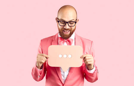 Positive funny man holding bubble talk sign with three dots isolated on pastel pink background....