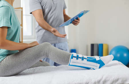 Crop closeup of doctor consult female patient with leg in bandage after injury or trauma. Physiotherapist appointment with client in rehabilitation center or clinic. Healthcare and rehab concept.の写真素材