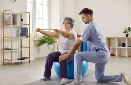 Medical specialist at modern rehabilitation center helping senior patient do physiotherapy exercises...