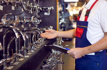 Choice of water taps and faucets. Male worker checks assortment on showcase with stainless steel...