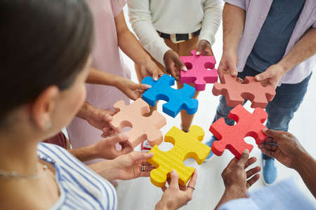 Diverse team of happy creative young multiracial people putting together colourful pieces of jigsaw...