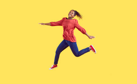 Happy black woman jumping in the studio. Positive carefree young Afro American girl wearing...