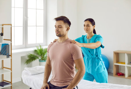 Female physiotherapist at modern physical therapy center helping male patient do rehabilitation...