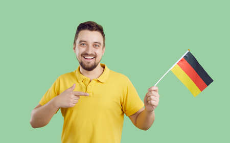 Happy man isolated on green color background holding flag of Germany. Cheerful handsome bearded...