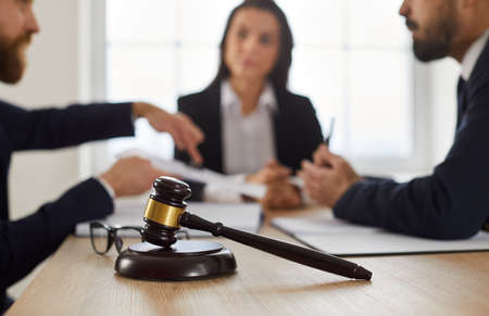 Close up of judges gavel on desk, with lawyer or attorney meeting with group of angry complaining...