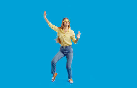 Smiling young woman isolated on blue studio background have fun dancing. Happy funny millennial teen...