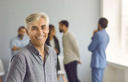 Portrait of happy successful mature business leader and company owner. Positive handsome white haired senior Caucasian man looking at camera and smiling standing against blurred office backgroundの写真素材