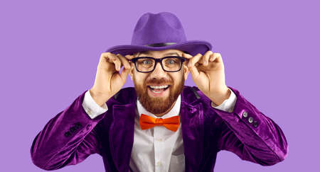 Portrait of funny cheerful stylish showman who wears glasses while standing on purple background. Caucasian bearded man in stylish purple jacket and hat is smiling madly looking at camera. Banner.の写真素材